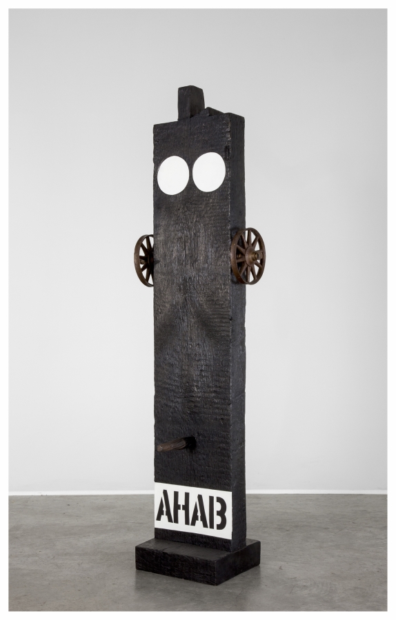 A black painted bronze beam shaped sculpture on a black wooden base. Across the bottom the work's title, Ahab, is painted in black stenciled letters against a white band of paint. Above the title is a wooden peg. A small wheel has been attached to both the right and left side of the upper third of the sculpture. At the top of the sculpture are two white circles.
