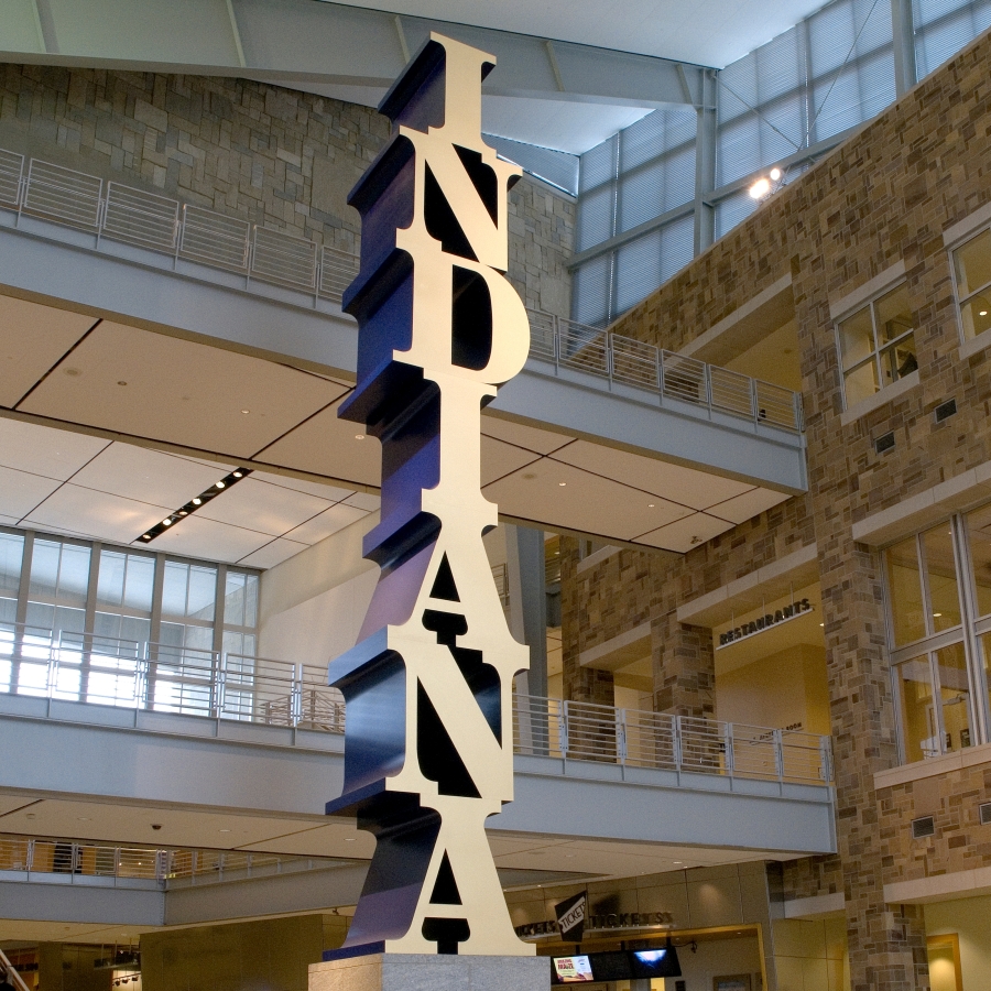 The Indiana Obelisk is a 575 1/4 inch high, with base, polychrome aluminum sculpture spelling the word Indiana vertically, starting with the I on top and ending with the A on the bottom. The letters have gold faces and blue sides.
