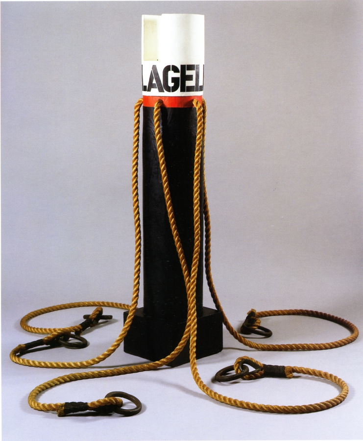 A 63 1/3 inch high wooden column on a wooden base. The top of the column has been painted white, with the work's titled, Flagellant, painted in black stenciled letters. Below the title is a red band, where four long ropes have been attached to the work.
