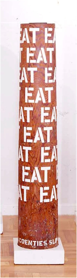 A column with nine rows of the word eat in gesso stenciled letters wrapping around the upper three quarters of the sculpture. 