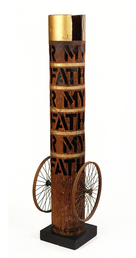 Column with its title "My Father" painted in five rows around the column in black stenciled letters. The top of the column is painted gold, and thin gold strips around the column separate each row of text. At the bottom of the column, on both sides, is a wheel.